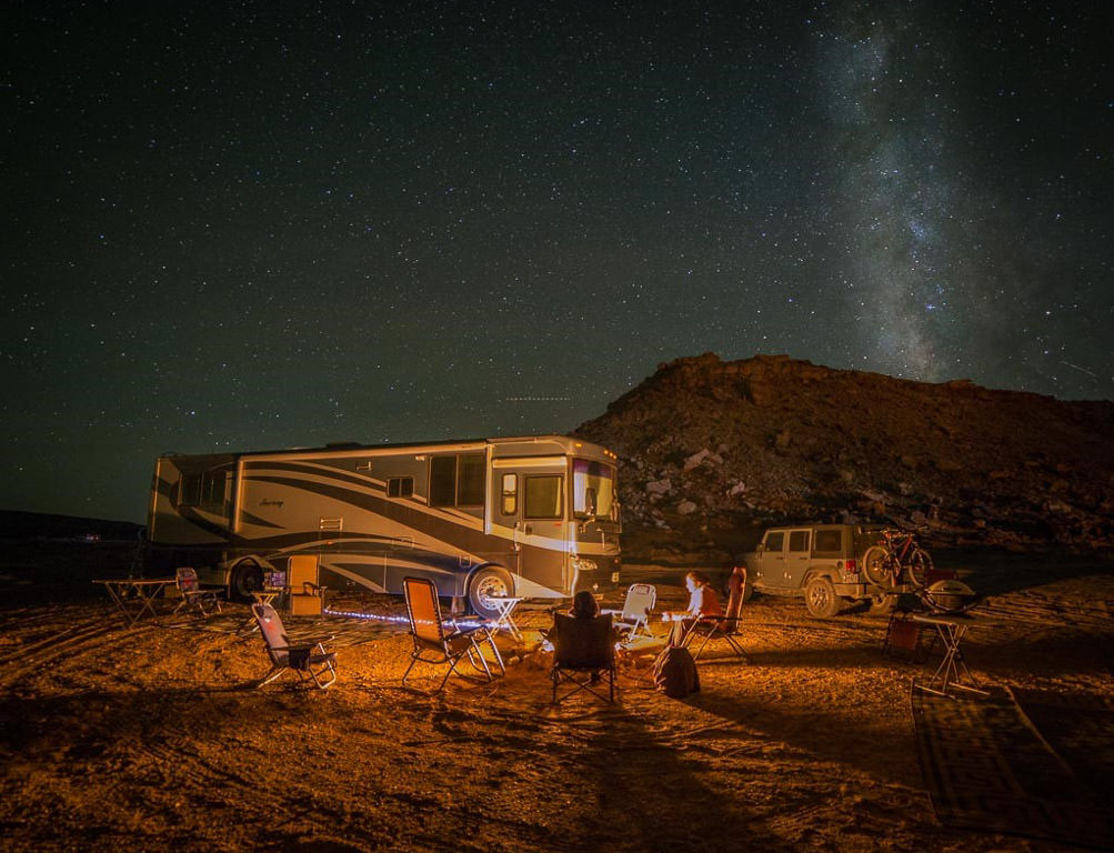 Winnebago Journey parked in rough landscape with stars overhead and campfire roaring