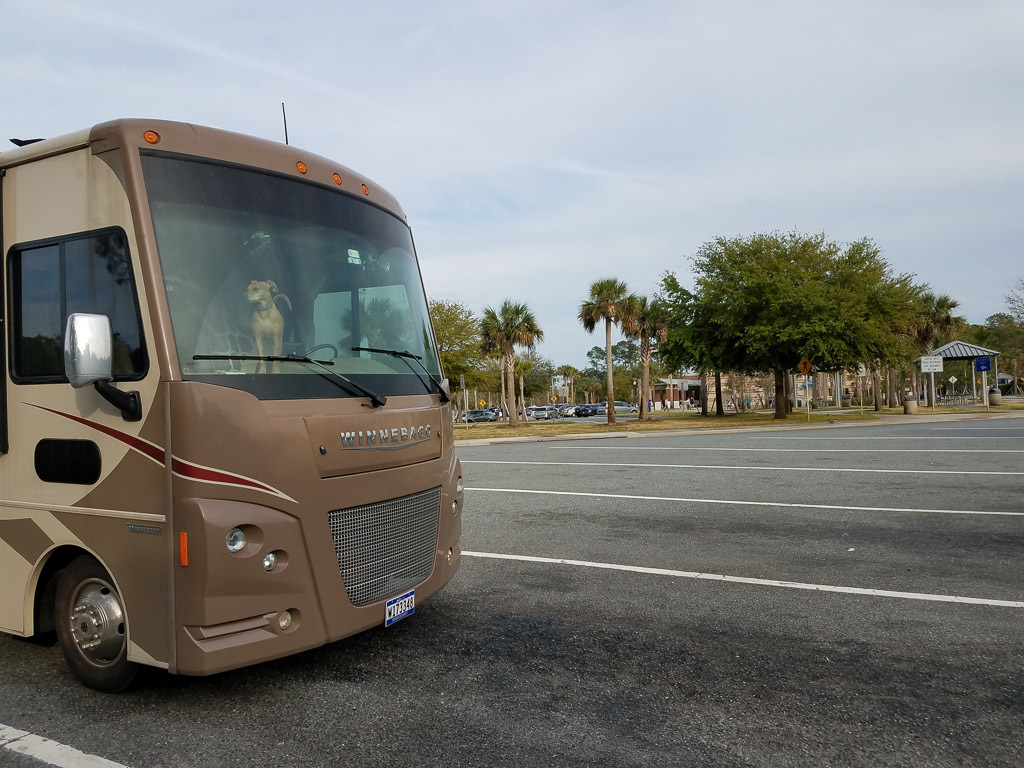 Winnebago motorhome parked in rest stop parking lot with dog standing on the dash