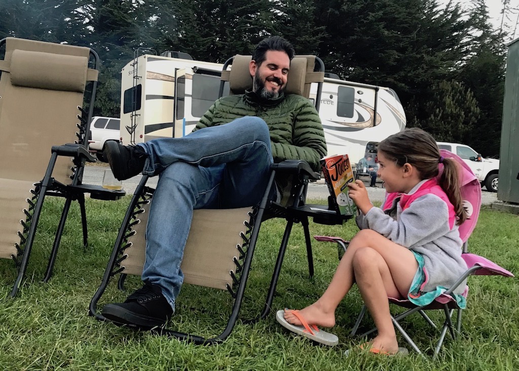 David and child sitting next to campfire reading joke book