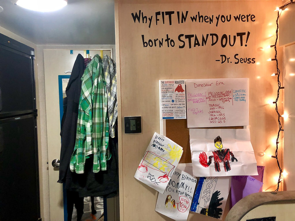 Wall with vinyl sticker quote and cork board with artwork on it. 