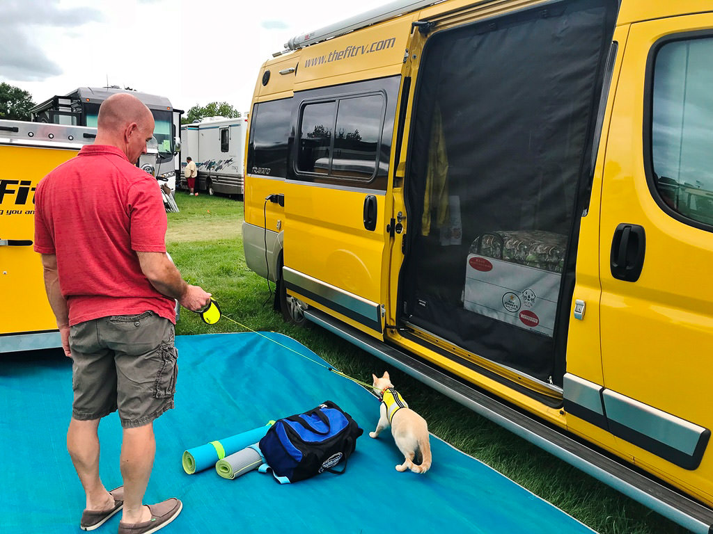 James with their cat outside their yellow Winnebago Travato
