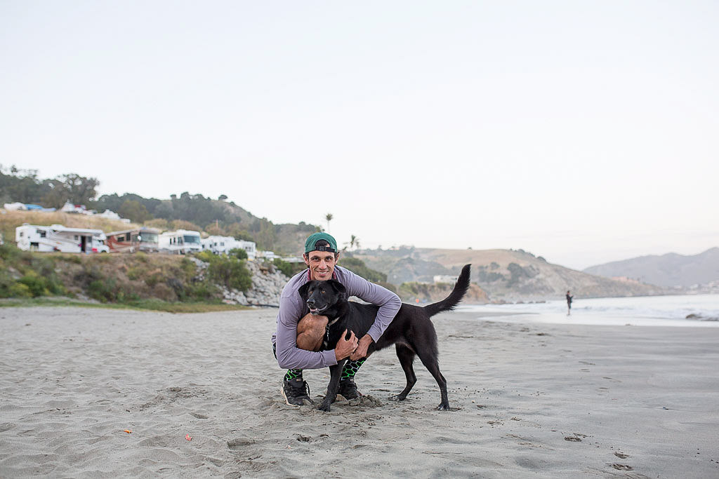 Jordan hugging their dog on a sandy beach