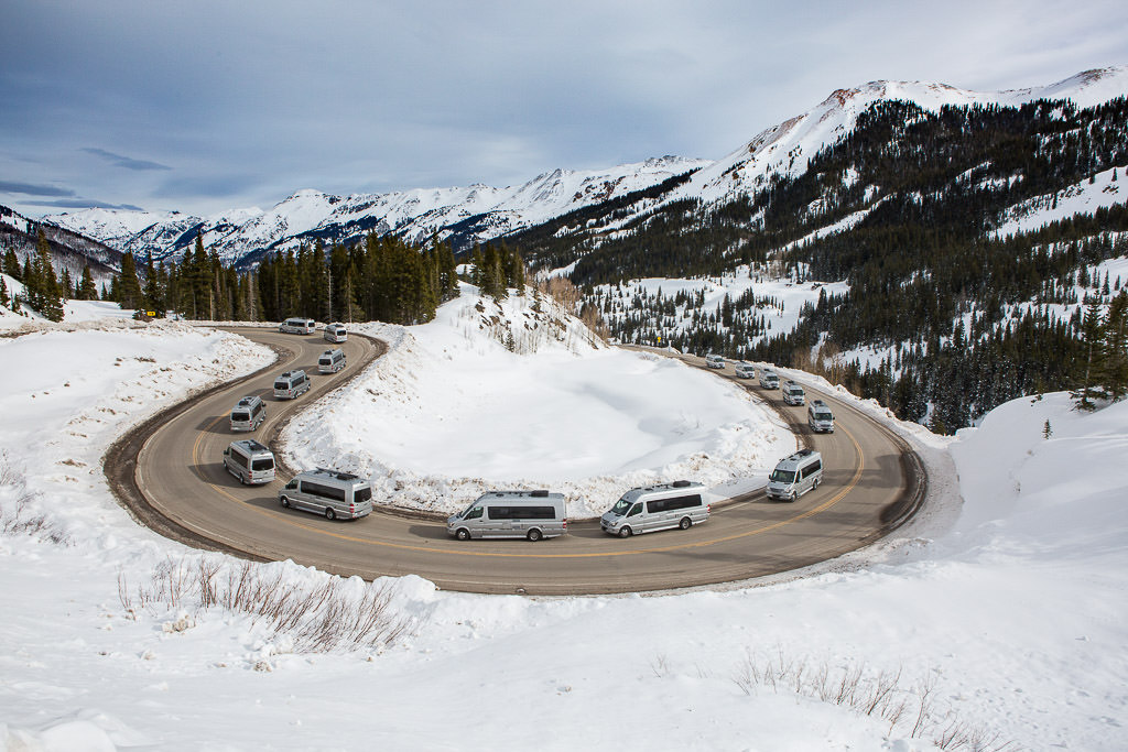 Line of vans driving around a winding paved road.