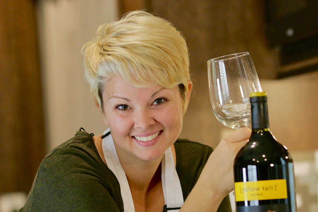 Jess holding a wine glass next to a bottle of wine