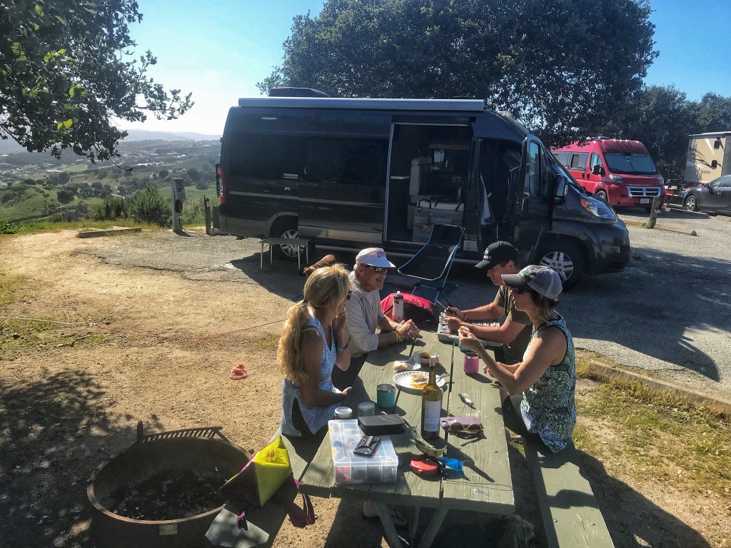 Four Winnebago camping attendees sitting at a picnic table eating outside of Travato
