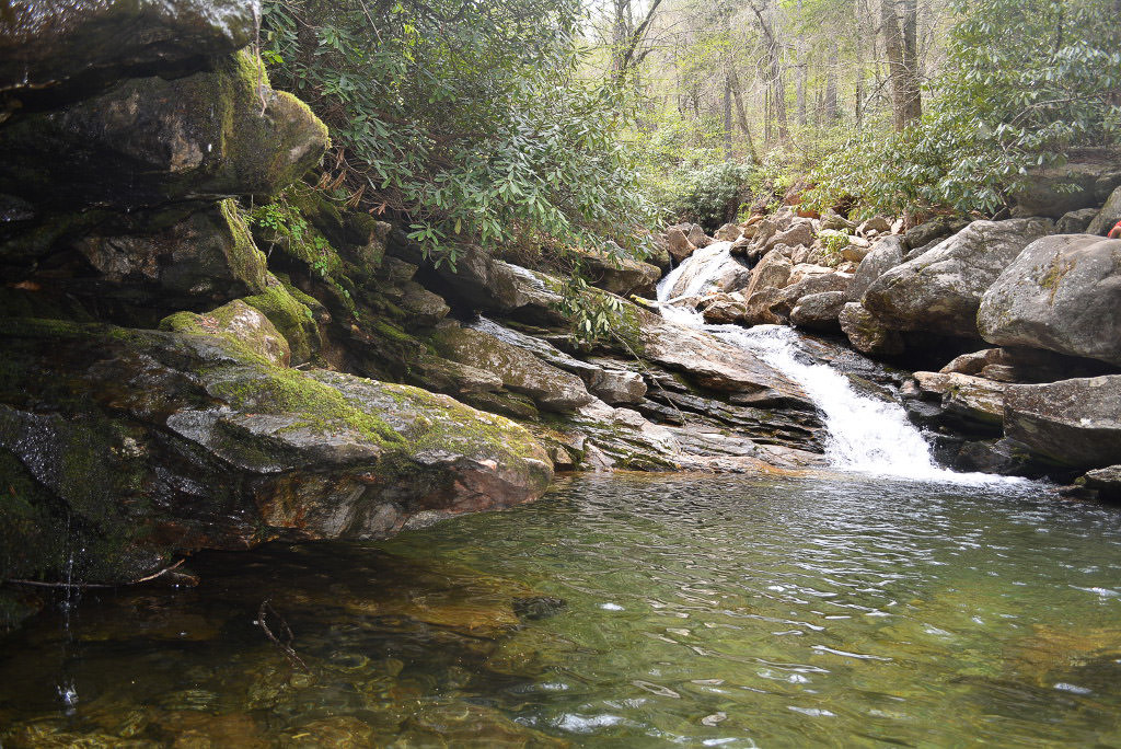 Stream rushing over rocks into a still pond.