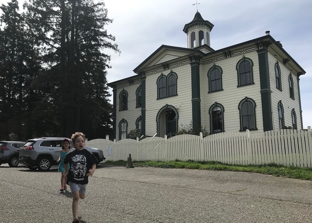 Two kids running in front of old house with white siding and black trim.