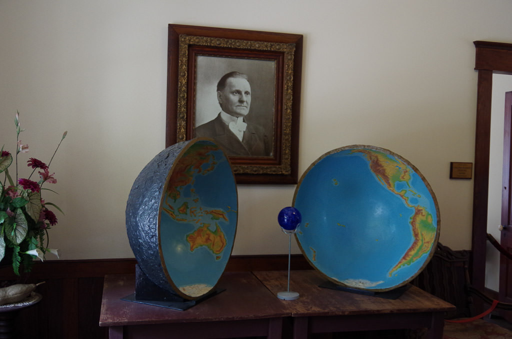 Diagram showing Dr. Cyrus Teed's theory that the universe existed on inside of a hollow Earth with his photo hanging on the wall behind.