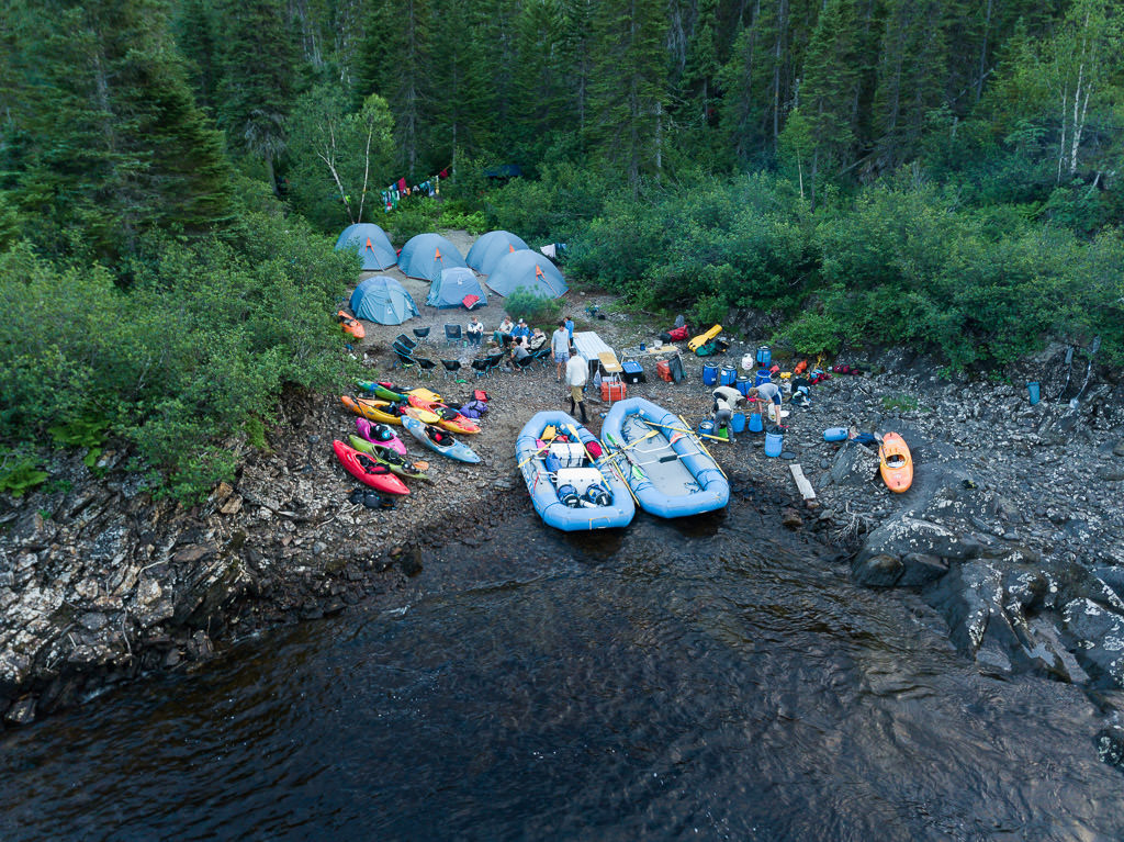 Group with tents set up, kayaks along the shore and chairs set up.