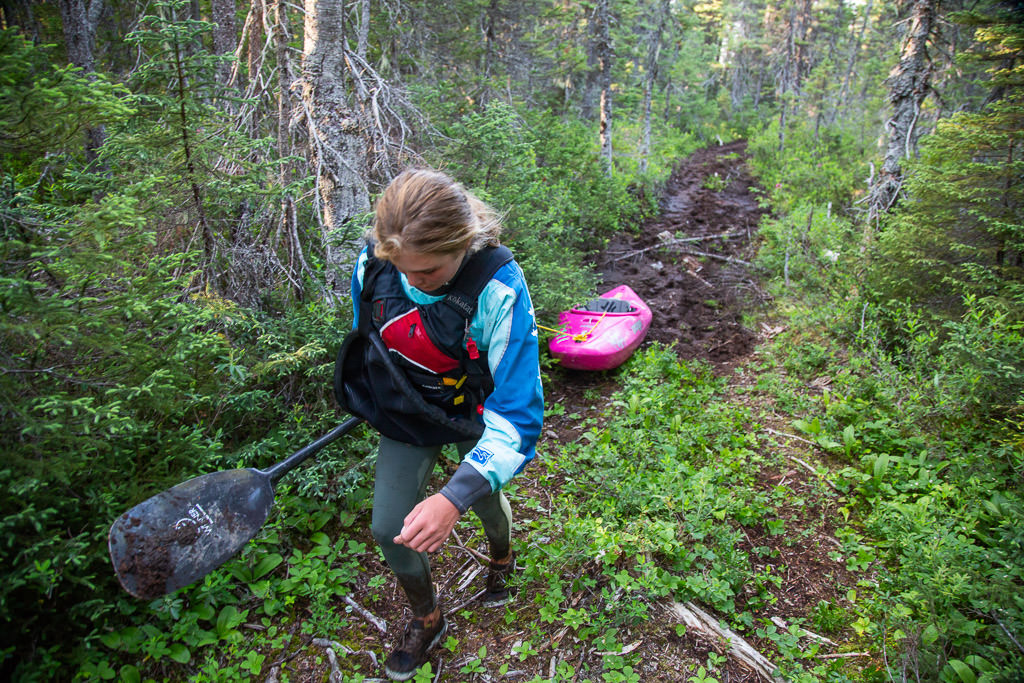 Abby pulling her kayak along a grassy and muddy trail.