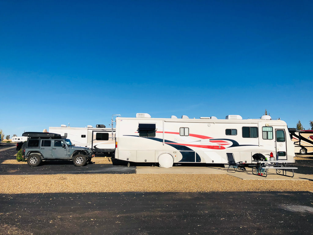 Tiffin Phaeton with tow car behind it in parking pad at a campground.