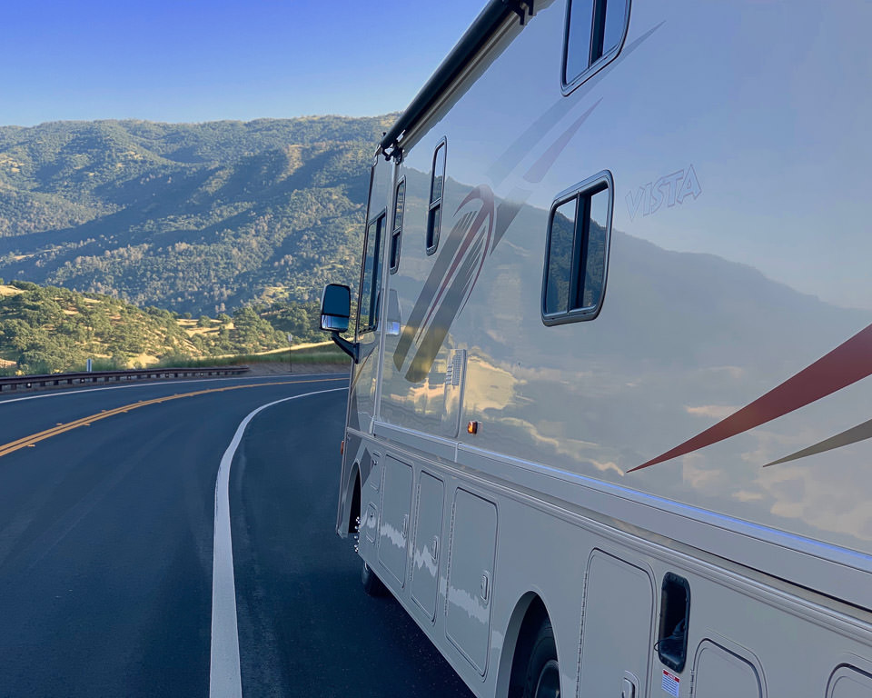 Winnebago Vista parked on the side of the road with tree covered hillside ahead. 