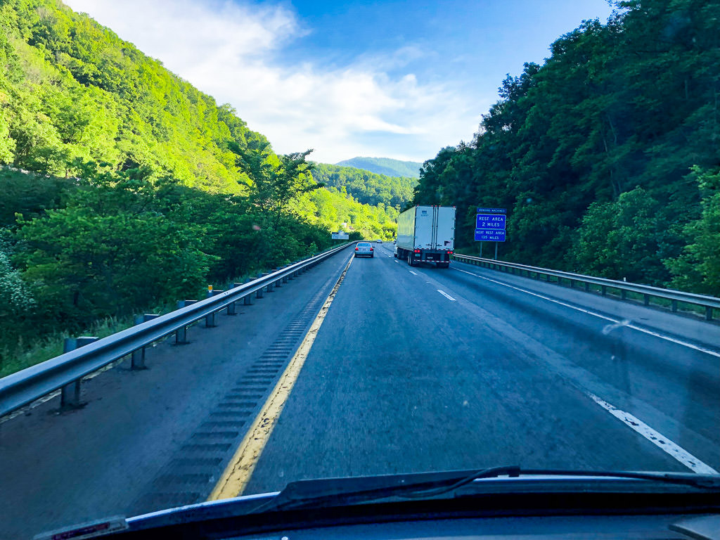 Highway with green tree filled hillsides on either side.