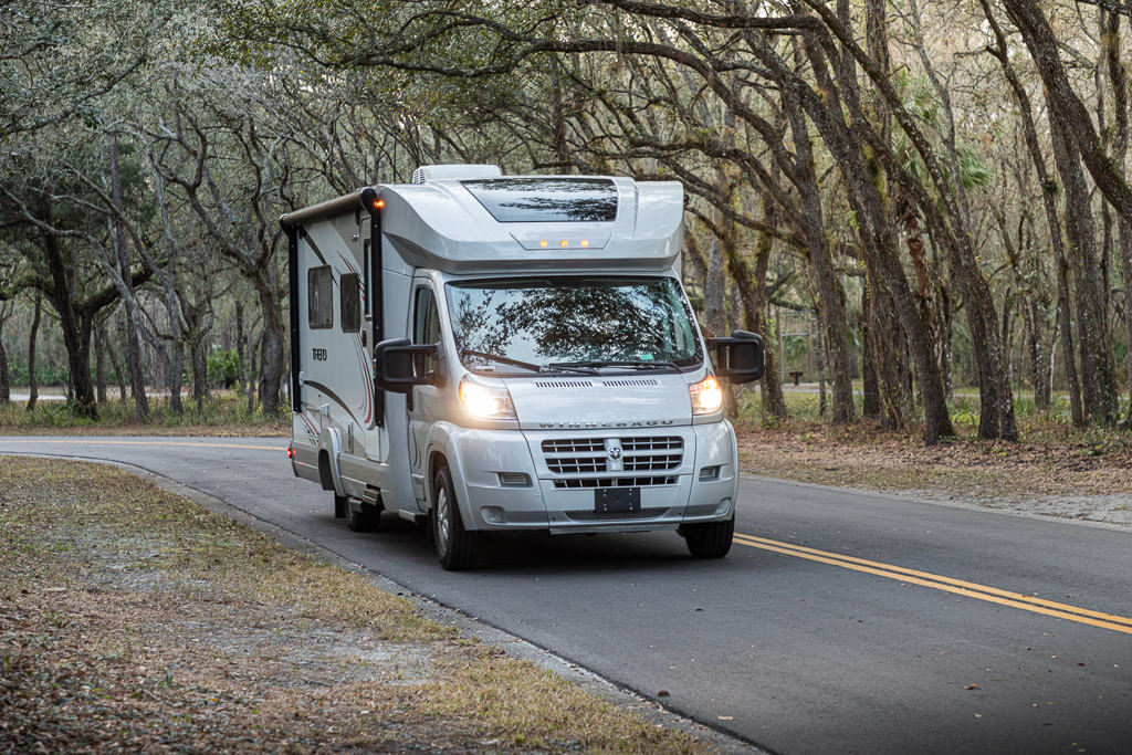 Winnebago Trend driving along tree lined road.