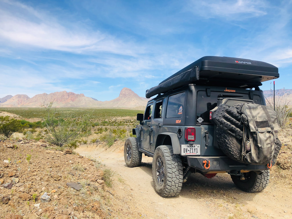 Jeep parked on gravel path looking out over rough rock formations in sight.