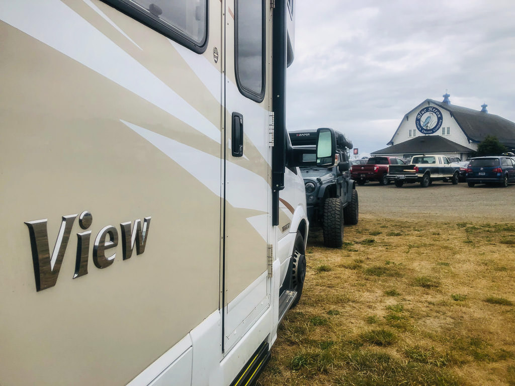 Winnebago View and jeep parked in parking lot in front of Blue Heron French Cheese Company buidling.