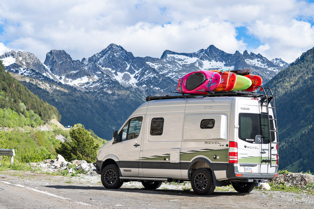 Winnebago Revel parked at the edge of a lookout with snow capped mountains in view.