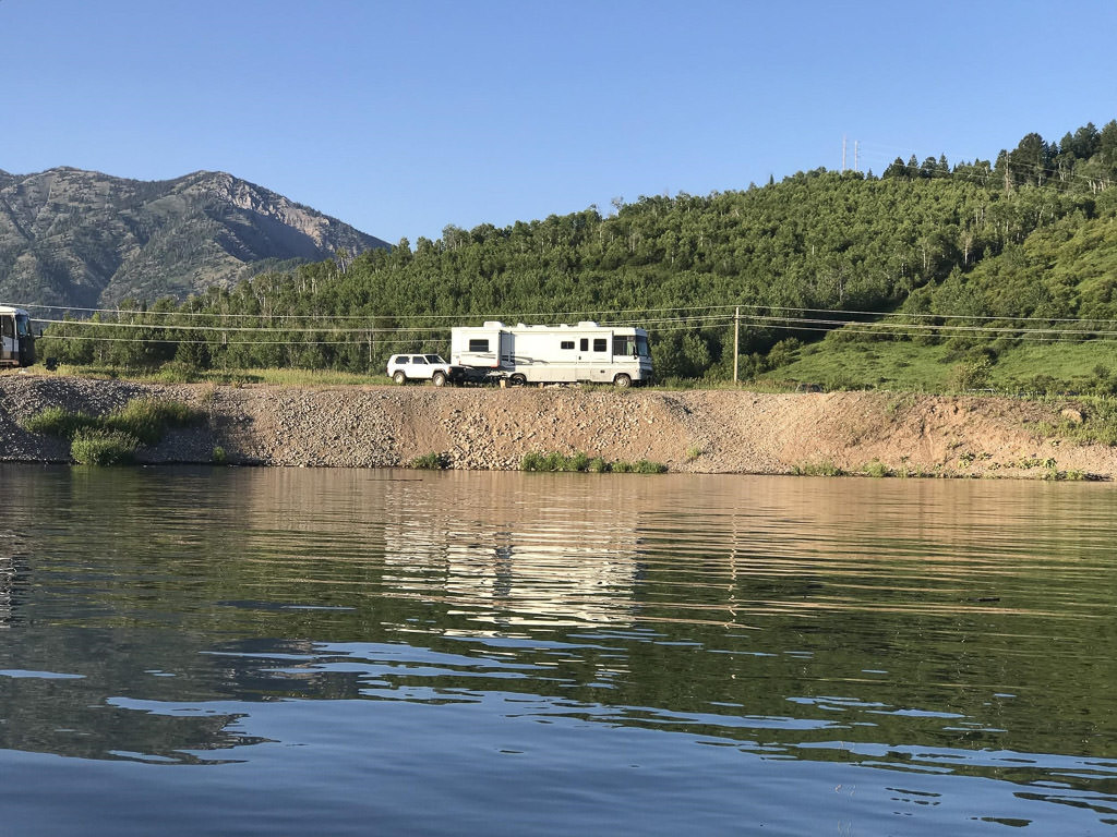Winnebago Brave with tow vehicle attached parked along body of water. 