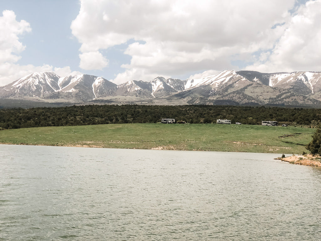 RVs parked near body of water with mountains in the background.