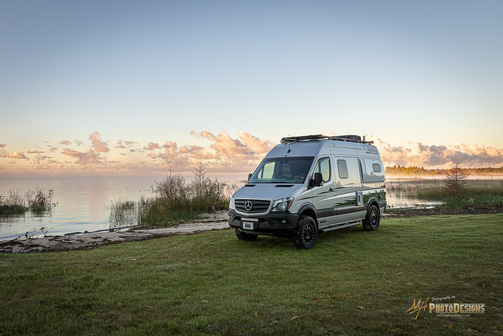 Winnebago Revel parked on grass right next to body of water.